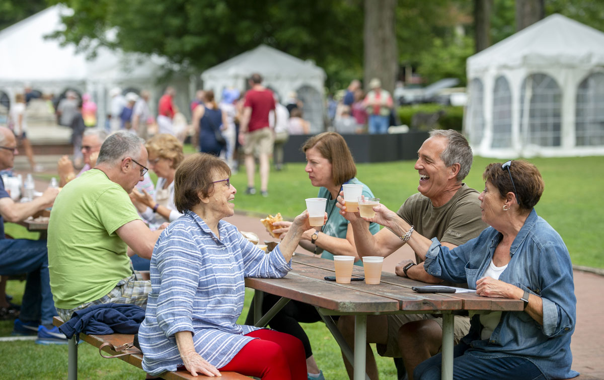 People gathered around a picnic table eating and drinking at the Chautauqua Food Festival