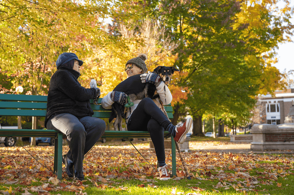 Two women and a dog sitting on a bench in Bestor Plaza during the fall