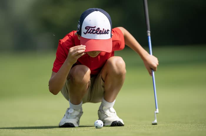 A boy crouching down to a golf ball
