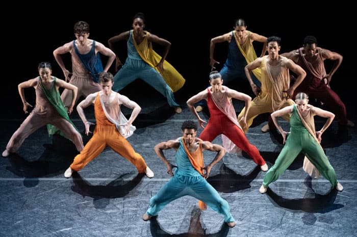 BalletX dancers performing in colorful costumes with hands on their hips on stage.