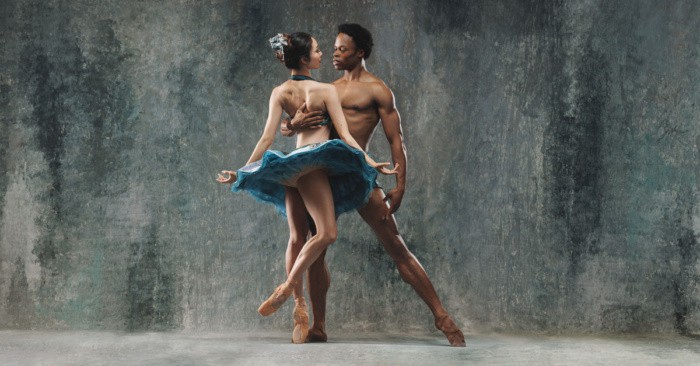 Two ballet dancers posing together in front of a blue gray background