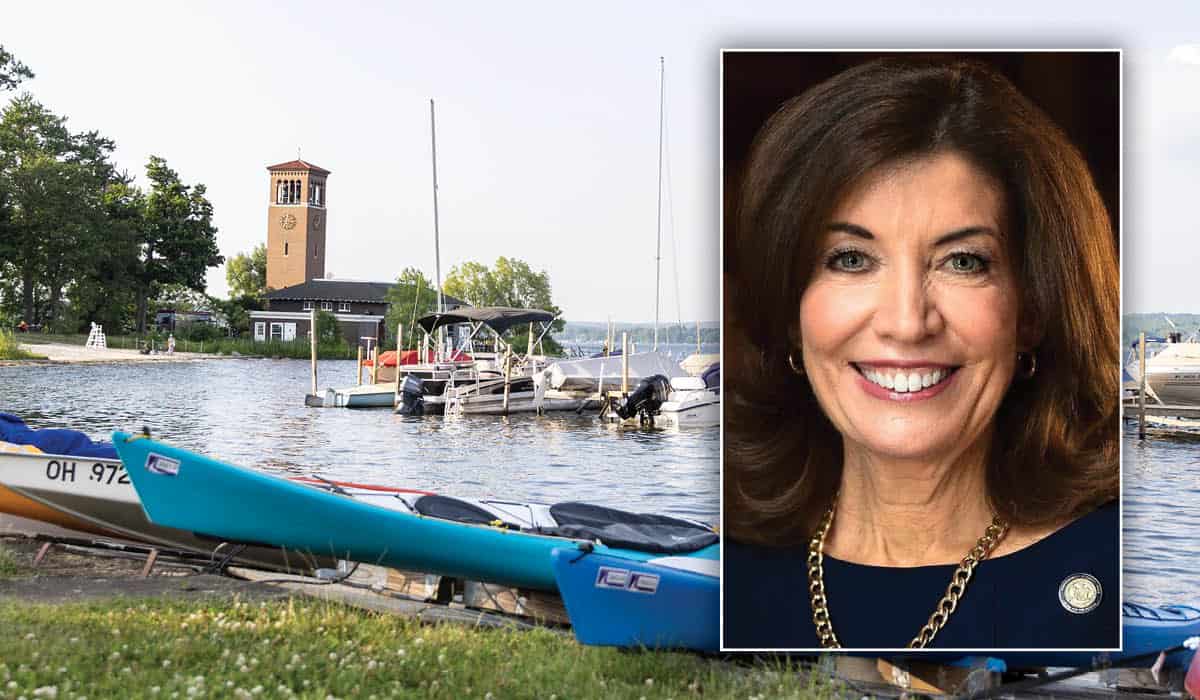 Kathy Hochul's headshot over a photo of Miller Bell Tower on Chautauqua Lake with kayaks and boats.