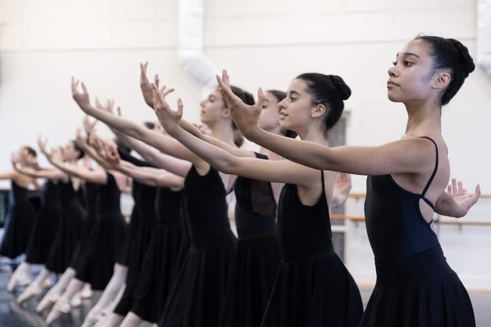 Dancers lined up with arms raised during a ballet class