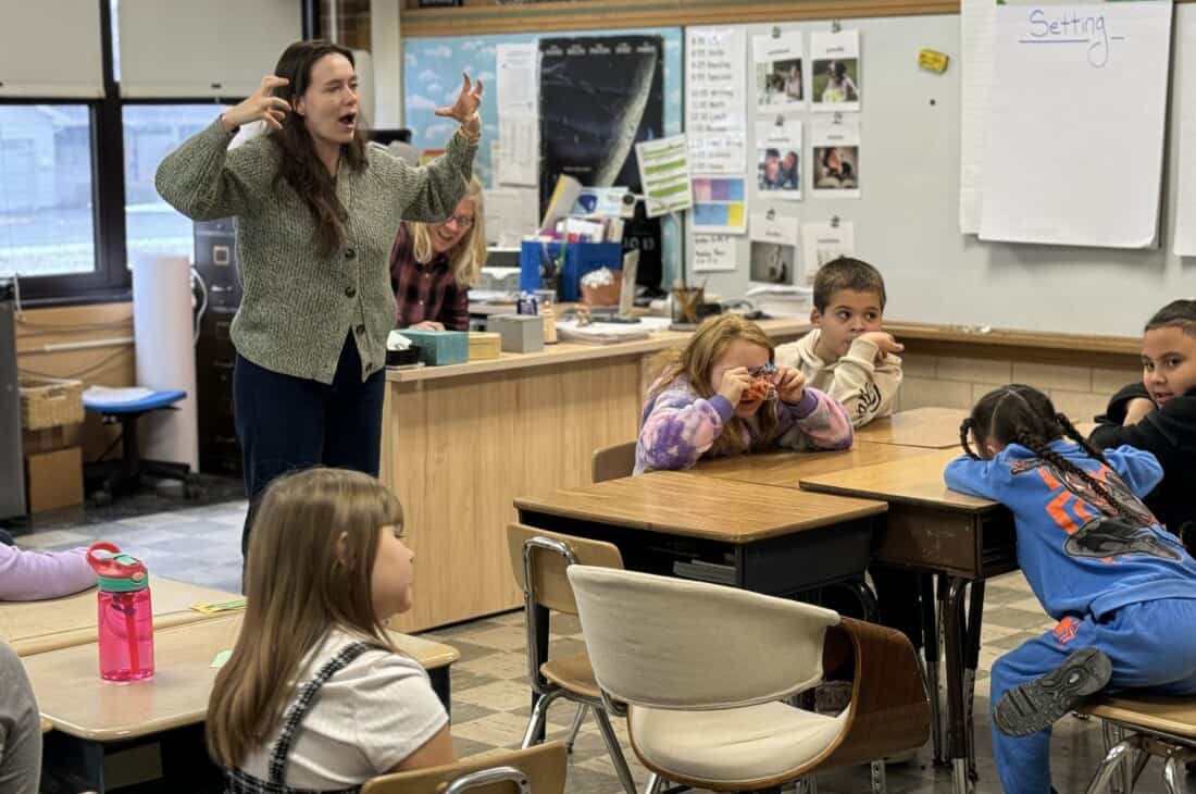 A teacher raising her hands while discussing development of a character in a classroom of children