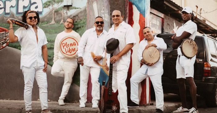 Plena Libre dressed in white and posing with their instruments