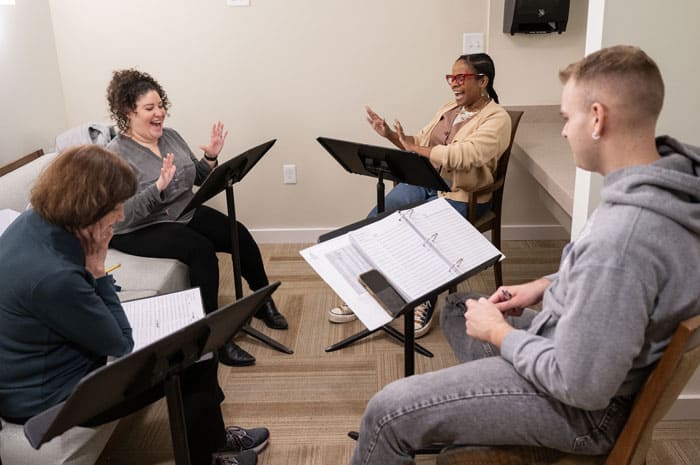 A group of four volunteers rehearsing a play with music stands in front of them