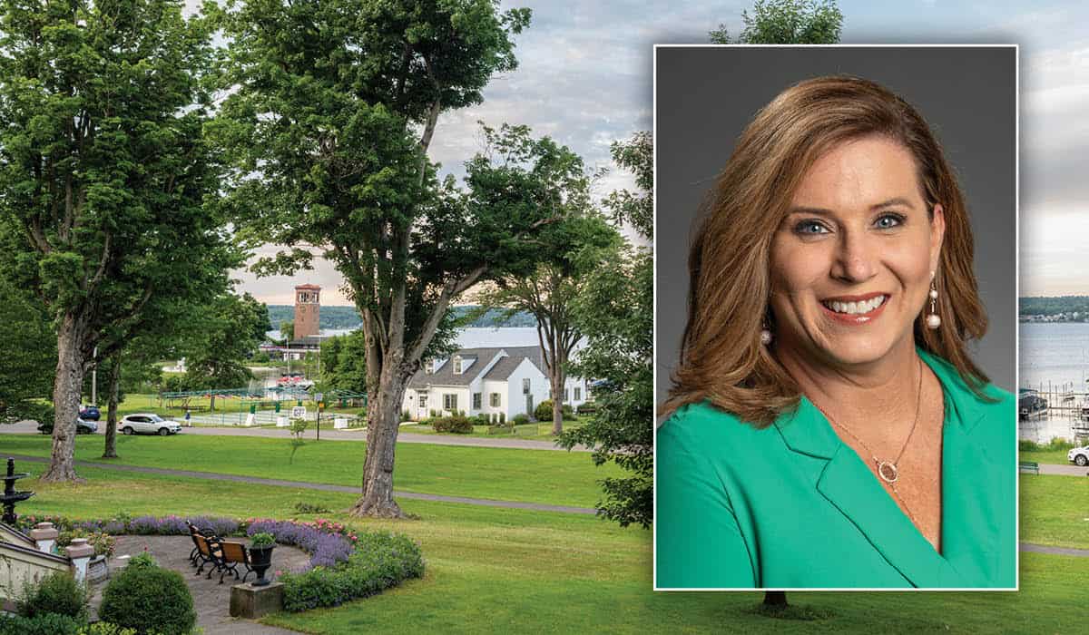 A headshot of Jill McCormick in a green blazer over top of a view of the Athenaeum Hotel lawn with Sports Club and Miller Bell Tower in the background