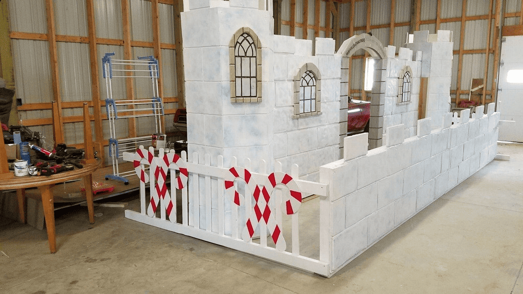 White wooden castle made to look as though it is comprised of ice sits in barn awaiting to be used and decorated. 