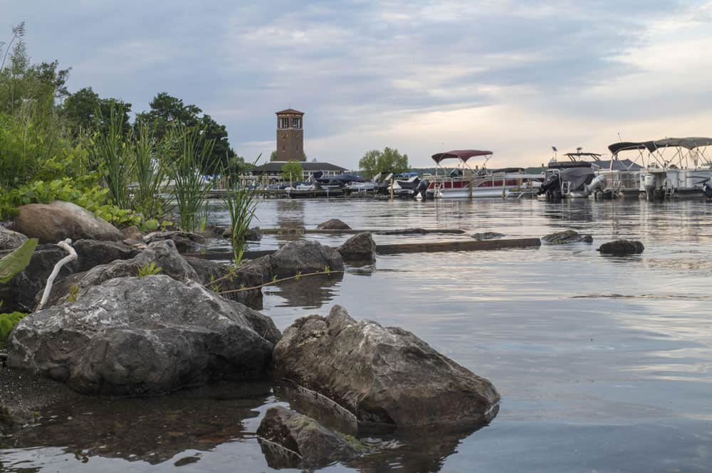 A view of Chautauqua Lake with rocks and boats in the foreground and Miller Bell Tower in the background