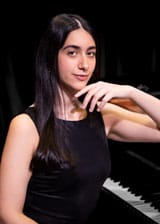 Yali Levy Schwartz in a black dress resting her elbow on a piano