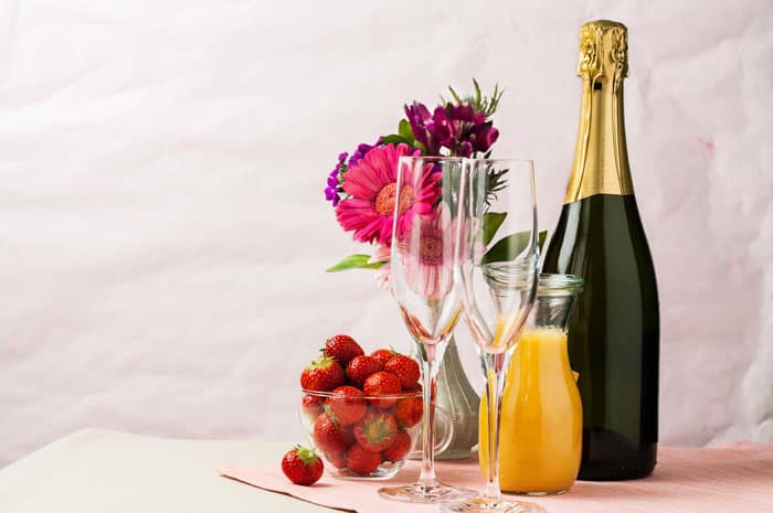A display of champagne, orange juice, champagne glasses, strawberries and flowers