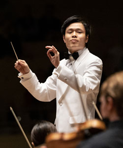 Ryo Hasegawa in a white suit conducting the Music School Festival Orchestra