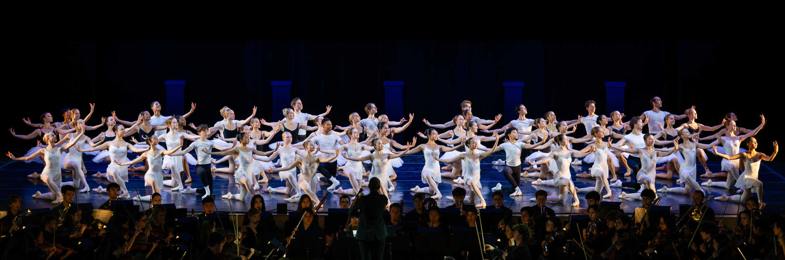 A group of dancers posing on stage with an orchestra