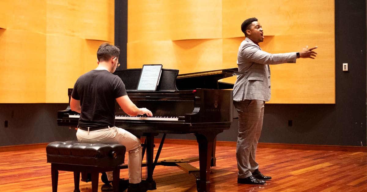 A man singing next to someone playing the piano